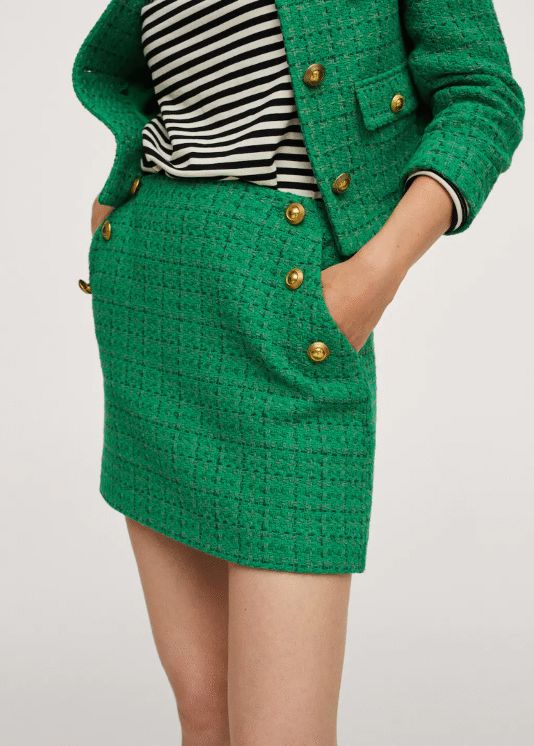Person wearing a green tweed skirt and jacket with gold buttons, hands in pocket.