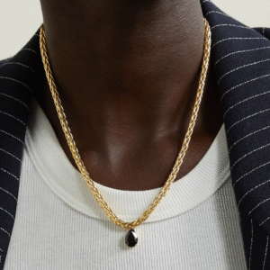 Person wearing a gold chain necklace with a dark pendant, white shirt, and pinstripe jacket.
