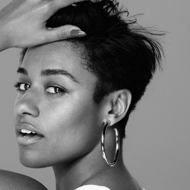 Person with short hair and hoop earring touches their forehead. Black and white.