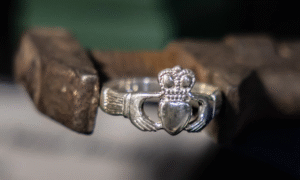 Claddagh ring with a heart, crown, and hands, held in a metal clamp.