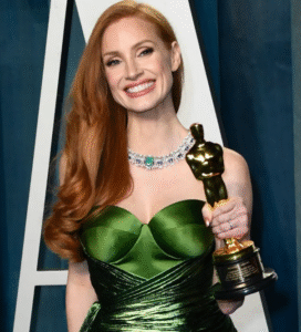Person in green dress holds an Oscar statue.