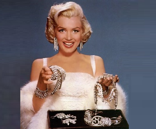 Person in white dress holds out sparkling jewelry over a display case.