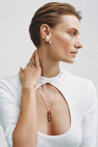 Person in white top with cutout, wearing jewelry, hand on neck, looking to the side.