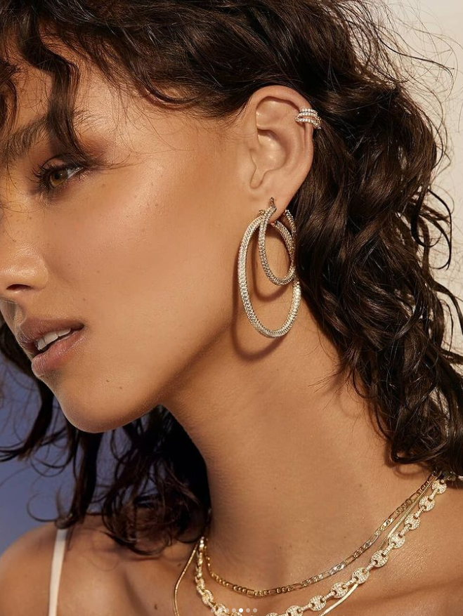 Person wearing hoop earrings and a cuff earring. Layered necklaces are visible.