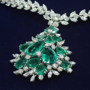 Necklace with white diamonds and pear-shaped green emeralds on a dark blue background.